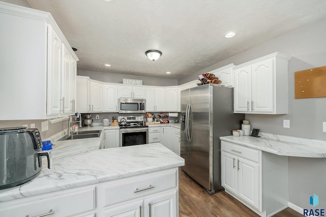 kitchen with kitchen peninsula, appliances with stainless steel finishes, dark wood-type flooring, sink, and white cabinetry