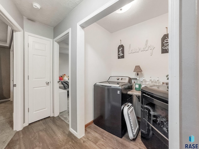 clothes washing area with wood-type flooring, separate washer and dryer, and a textured ceiling