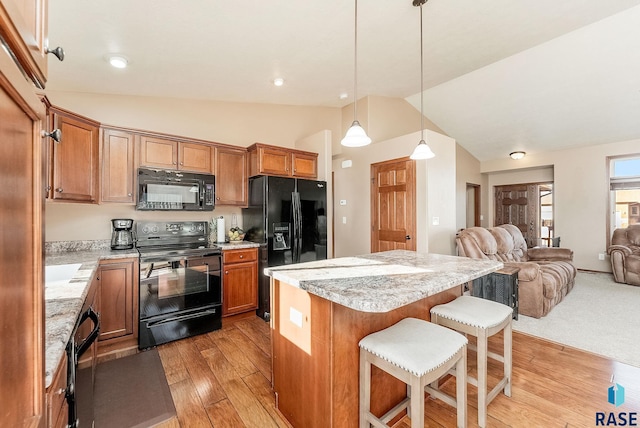 kitchen with hanging light fixtures, vaulted ceiling, a breakfast bar, black appliances, and light wood-type flooring