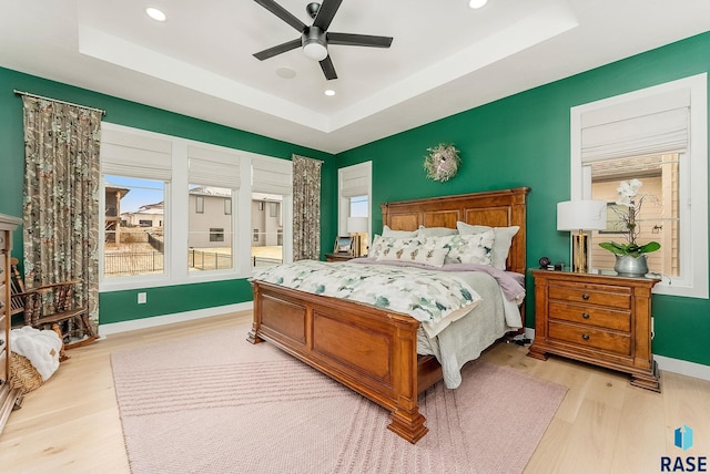 bedroom featuring light wood-type flooring, a tray ceiling, baseboards, and recessed lighting