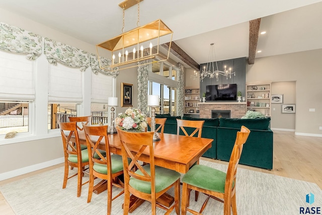 dining area featuring light wood-style floors, a brick fireplace, beamed ceiling, and baseboards