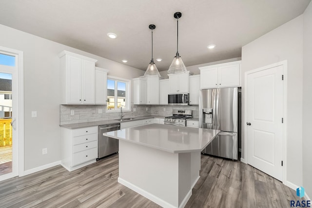 kitchen featuring white cabinetry, sink, stainless steel appliances, pendant lighting, and a kitchen island