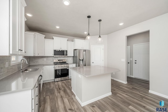 kitchen featuring stainless steel appliances, sink, pendant lighting, white cabinets, and a center island