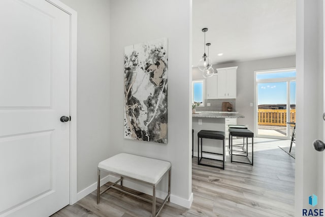 interior space featuring tasteful backsplash, white cabinetry, hanging light fixtures, light stone counters, and light hardwood / wood-style floors