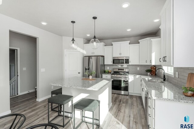 kitchen with sink, light stone counters, a kitchen island, stainless steel appliances, and white cabinets