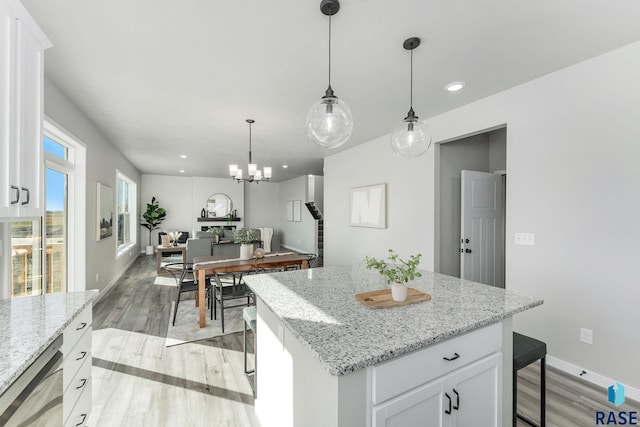 kitchen with white cabinetry, a kitchen island, light stone countertops, and decorative light fixtures