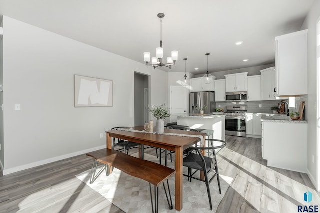 dining space featuring light wood-type flooring, an inviting chandelier, and sink