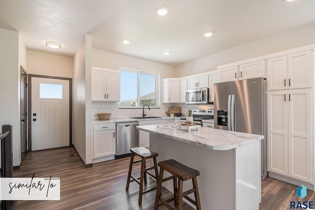 kitchen with appliances with stainless steel finishes, white cabinets, a kitchen island, and sink