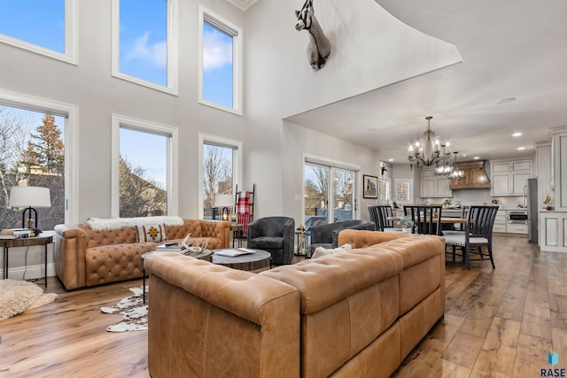 living room with light hardwood / wood-style flooring, a high ceiling, plenty of natural light, and an inviting chandelier