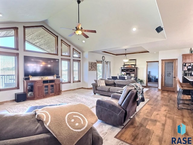 living room with a raised ceiling, ceiling fan, vaulted ceiling, and light wood-type flooring