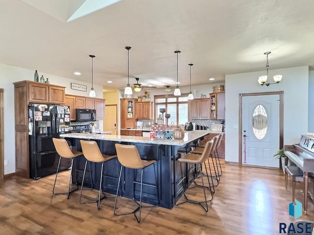 kitchen featuring hanging light fixtures, a spacious island, a breakfast bar area, decorative backsplash, and black appliances