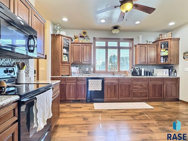 kitchen featuring light wood-type flooring, backsplash, ceiling fan, sink, and black appliances