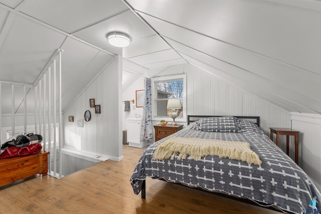 bedroom featuring wood walls, light hardwood / wood-style flooring, and vaulted ceiling