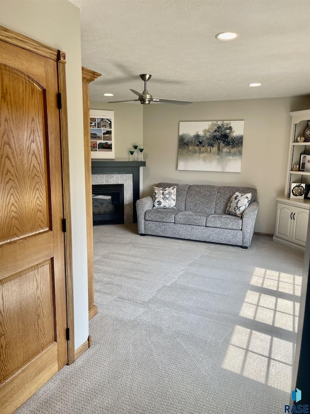 carpeted living room with ceiling fan and a tiled fireplace