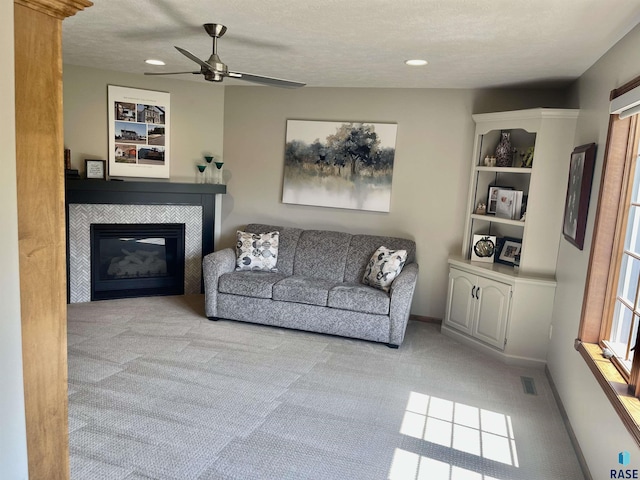 living room with ceiling fan, a fireplace, light colored carpet, and a textured ceiling