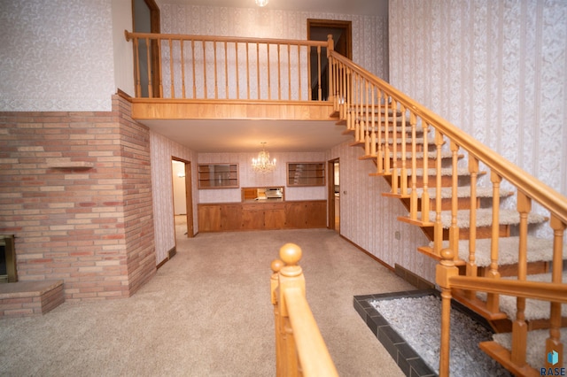 unfurnished living room featuring a fireplace, light carpet, a high ceiling, and a chandelier