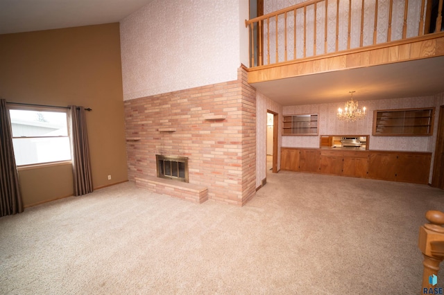 unfurnished living room featuring a chandelier, a towering ceiling, a brick fireplace, and carpet flooring