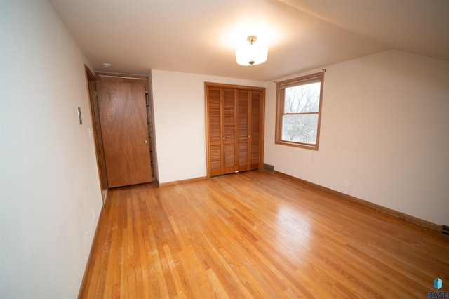 unfurnished bedroom featuring light wood-type flooring, a closet, and lofted ceiling