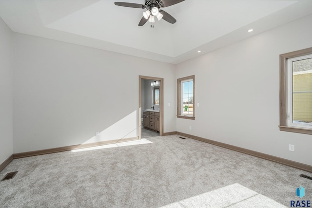 spare room featuring a tray ceiling, a wealth of natural light, ceiling fan, and light colored carpet