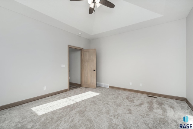 carpeted spare room with a tray ceiling and ceiling fan