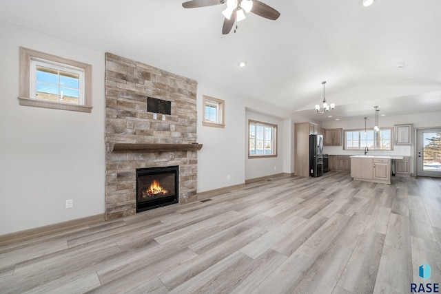 unfurnished living room with lofted ceiling, a stone fireplace, sink, light wood-type flooring, and a healthy amount of sunlight