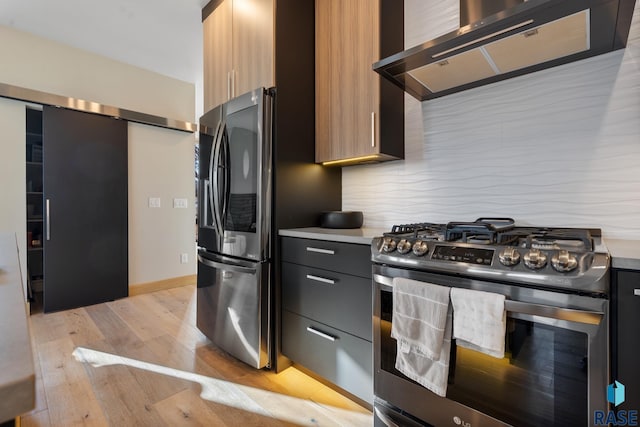 kitchen featuring stainless steel appliances, light countertops, light wood-style flooring, wall chimney range hood, and modern cabinets