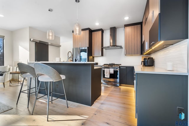 kitchen featuring decorative light fixtures, stainless steel appliances, light countertops, wall chimney range hood, and modern cabinets