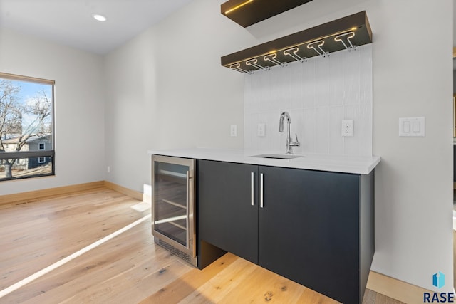 bar featuring light wood finished floors, beverage cooler, baseboards, a sink, and recessed lighting