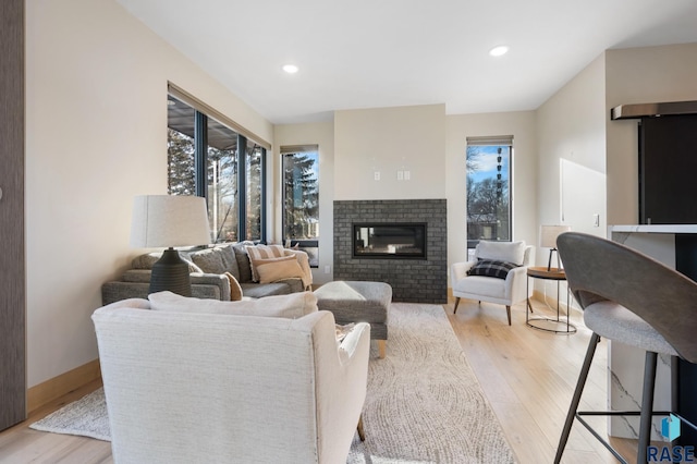 living area with light wood finished floors, a brick fireplace, and recessed lighting