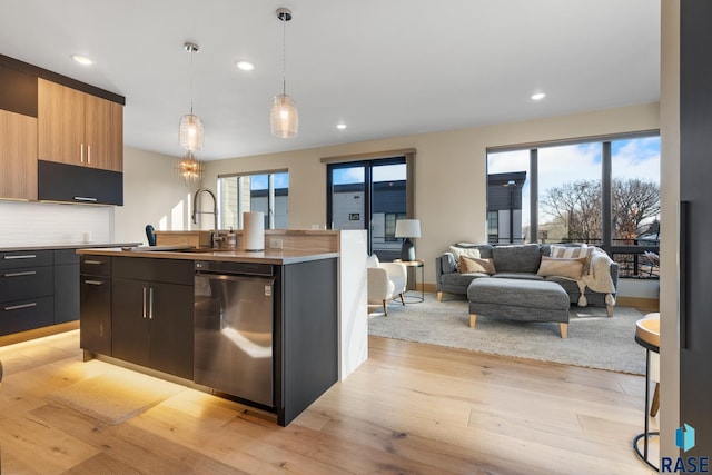 kitchen featuring dishwasher, an island with sink, open floor plan, hanging light fixtures, and light countertops