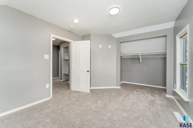 unfurnished bedroom with vaulted ceiling, a closet, light colored carpet, and a textured ceiling