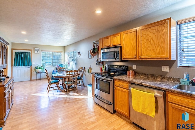 kitchen featuring appliances with stainless steel finishes, a textured ceiling, light hardwood / wood-style flooring, and sink