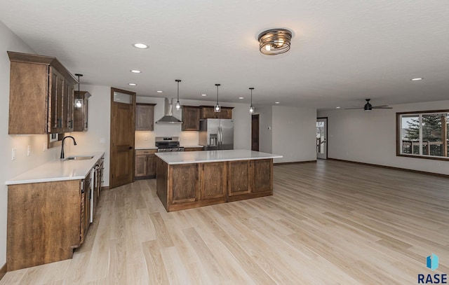 kitchen featuring sink, wall chimney range hood, decorative light fixtures, a kitchen island, and appliances with stainless steel finishes