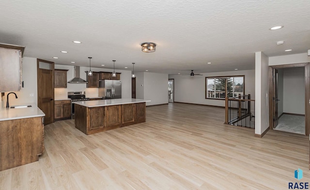 kitchen featuring wall chimney exhaust hood, stainless steel appliances, light hardwood / wood-style floors, a kitchen island, and hanging light fixtures