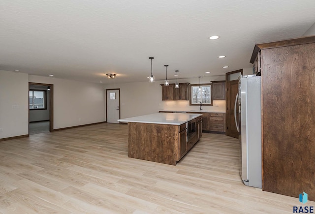 kitchen with sink, decorative light fixtures, a center island, light hardwood / wood-style floors, and fridge