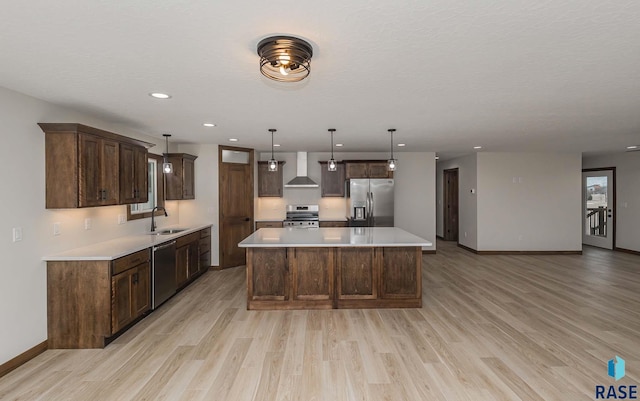 kitchen with wall chimney exhaust hood, stainless steel appliances, sink, a center island, and hanging light fixtures