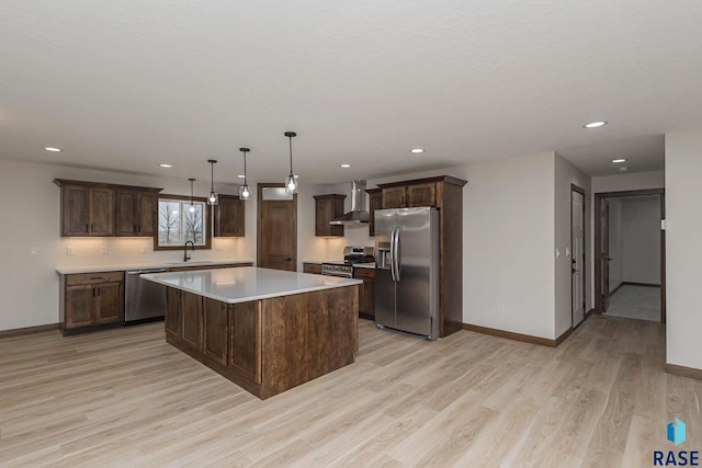 kitchen featuring sink, wall chimney range hood, pendant lighting, a spacious island, and appliances with stainless steel finishes