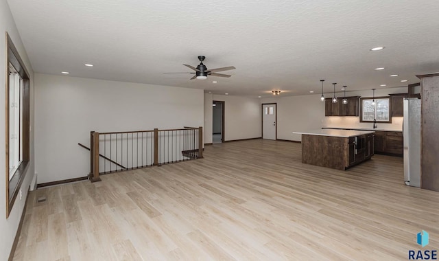 kitchen with light wood-type flooring, a textured ceiling, dark brown cabinetry, white refrigerator, and a center island