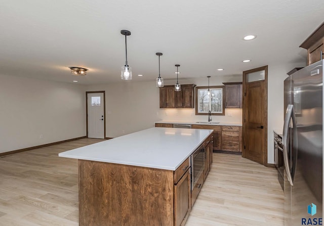 kitchen featuring sink, a center island, hanging light fixtures, appliances with stainless steel finishes, and light wood-type flooring