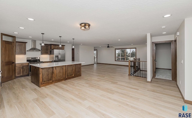 kitchen featuring pendant lighting, wall chimney range hood, light wood-type flooring, appliances with stainless steel finishes, and a kitchen island