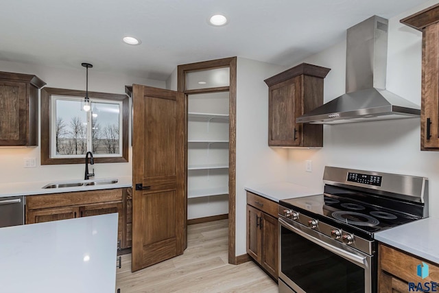 kitchen featuring sink, hanging light fixtures, wall chimney range hood, appliances with stainless steel finishes, and light wood-type flooring