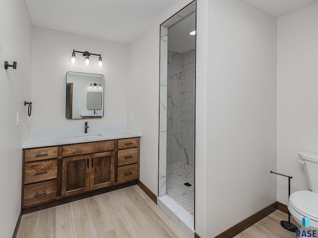 bathroom featuring hardwood / wood-style flooring, vanity, toilet, and tiled shower