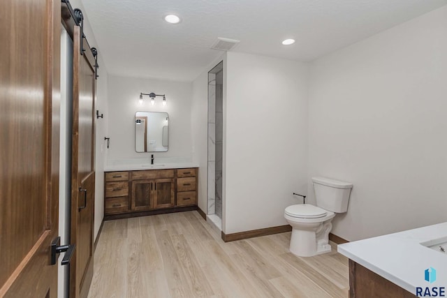 bathroom with walk in shower, vanity, a textured ceiling, wood-type flooring, and toilet