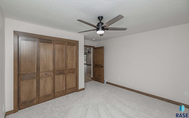 unfurnished bedroom with ceiling fan, a textured ceiling, light carpet, and a closet