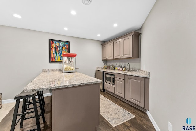 kitchen with light stone counters, sink, dark hardwood / wood-style floors, stainless steel microwave, and a breakfast bar area