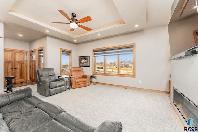 living room featuring carpet flooring, a raised ceiling, and ceiling fan