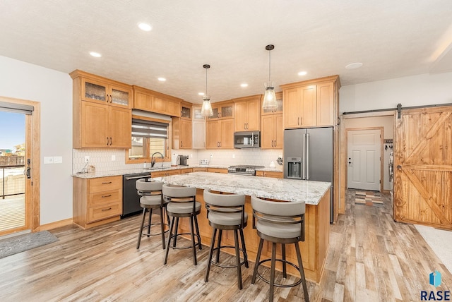 kitchen featuring appliances with stainless steel finishes, light wood-type flooring, sink, a barn door, and a kitchen island