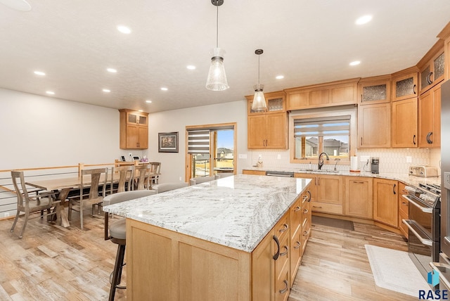 kitchen featuring sink, light hardwood / wood-style flooring, decorative light fixtures, a kitchen island, and light stone counters