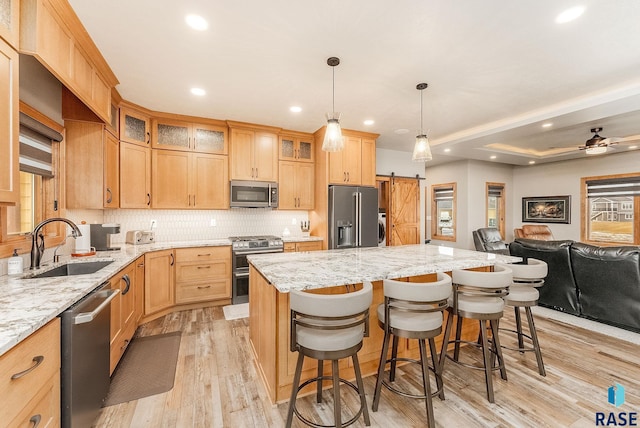 kitchen featuring appliances with stainless steel finishes, light wood-type flooring, light stone counters, a breakfast bar, and a barn door