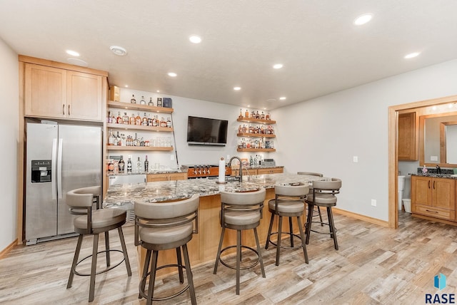 bar with stainless steel fridge, light stone countertops, sink, and light hardwood / wood-style flooring